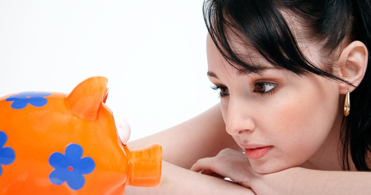 Photo of a girl attentively observing a piggy bank, reflecting the importance of financial awareness and saving money from a young age