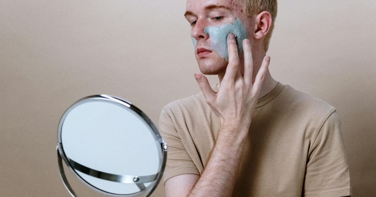 A man applying a beauty mask while looking in the mirror, highlighting the importance of taking time for self-care.