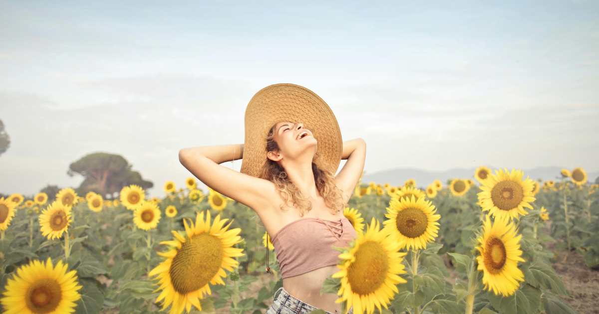 A woman laughs joyfully, face turned upwards, embodying the happiness of change and personal transformation amidst a sunflower garden.