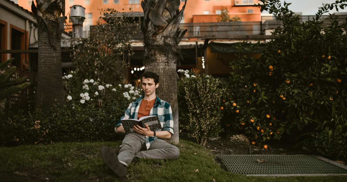 Image of a man sitting in a garden and reading a book, symbolizing daily encouragement for changing oneself through reading.