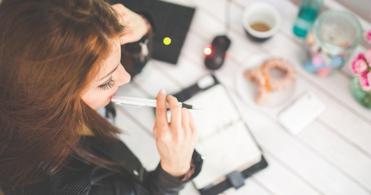 Focused woman at office desk, deep in thought while taking notes.