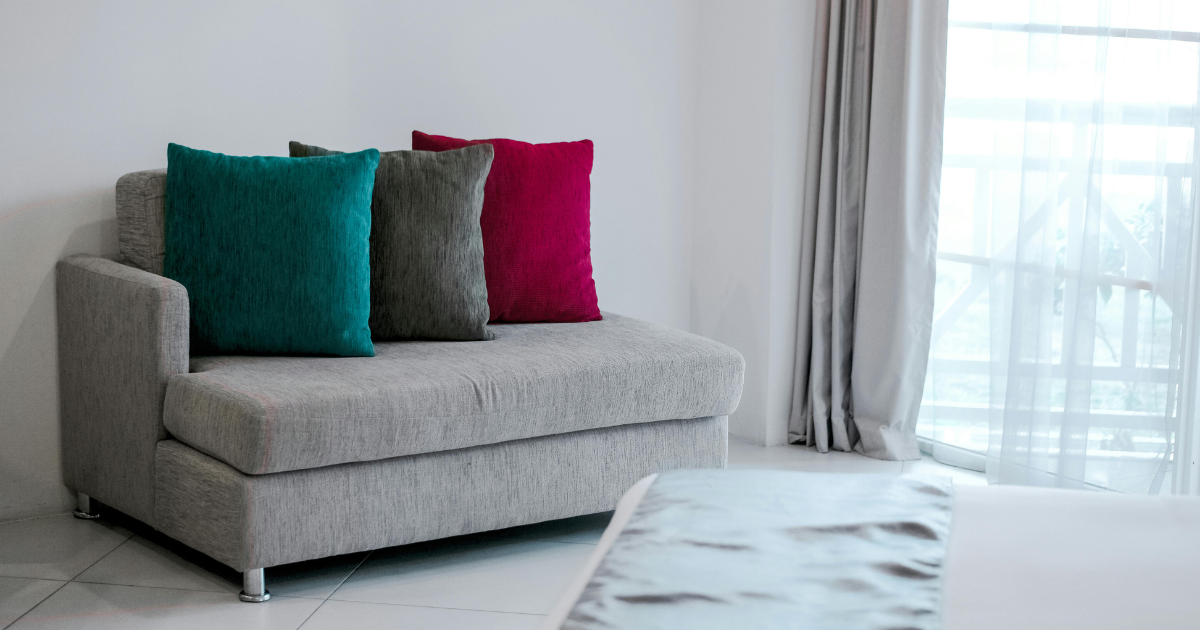 A single sofa in a minimalist living room, embodying sustainable minimalism, with a simple curtain in the background.