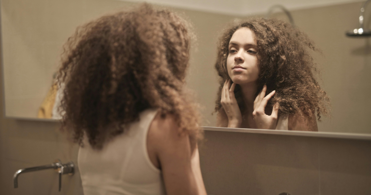 Woman gazes into mirror, contemplating change and transformation.