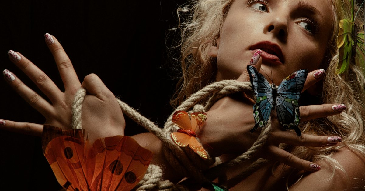 An intense-faced performer with hands tied by robes, surrounded by butterflies, symbolizing the desire for change and freedom metaphorically.