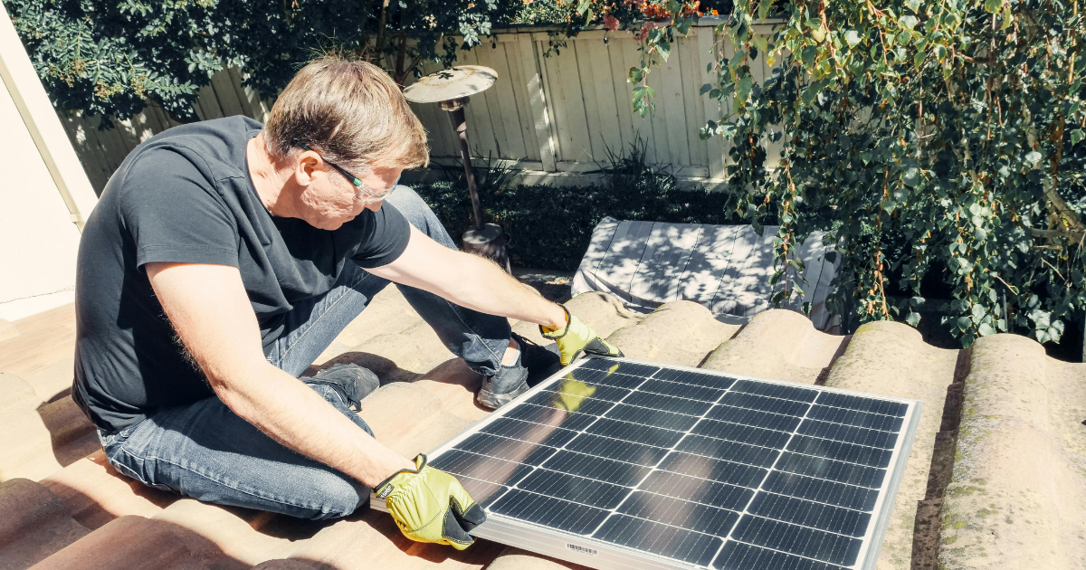 A man installing a solar panel in an off-grid living setup, demonstrating the fundamental aspect of self-sustainable living.