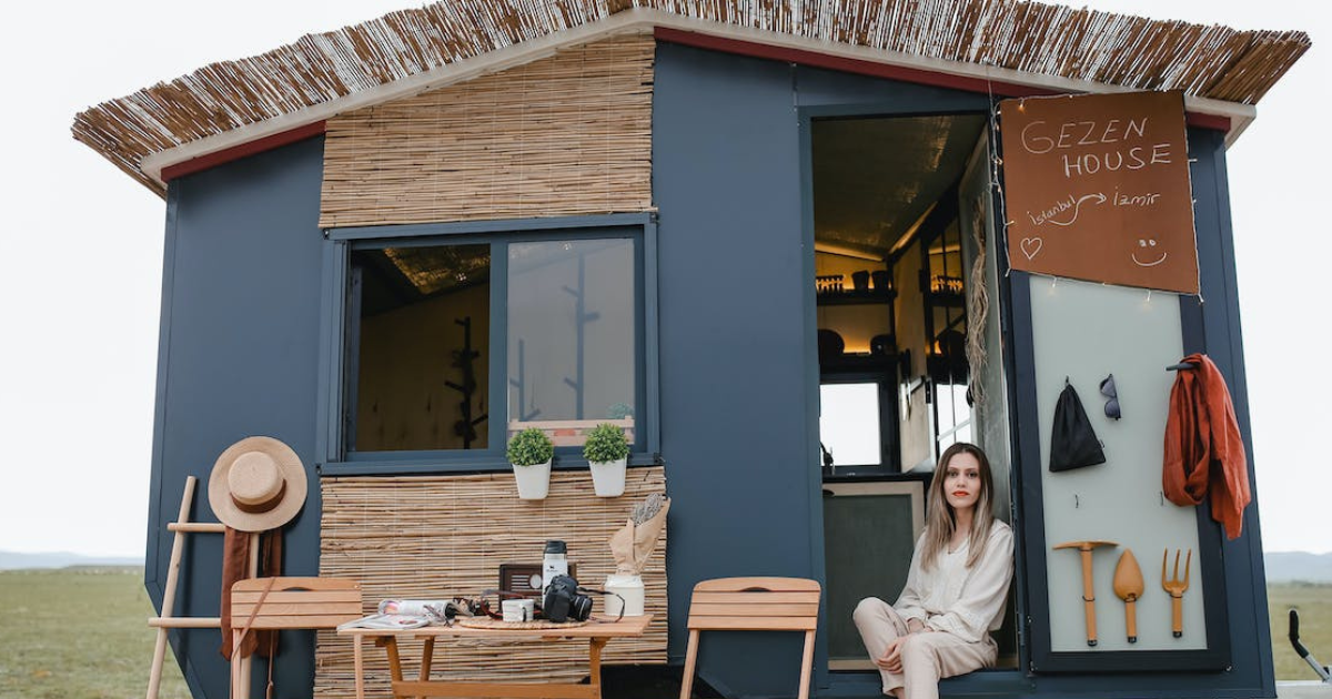 A woman sitting outside a cozy tiny house surrounded by essentials, showcasing off-grid living