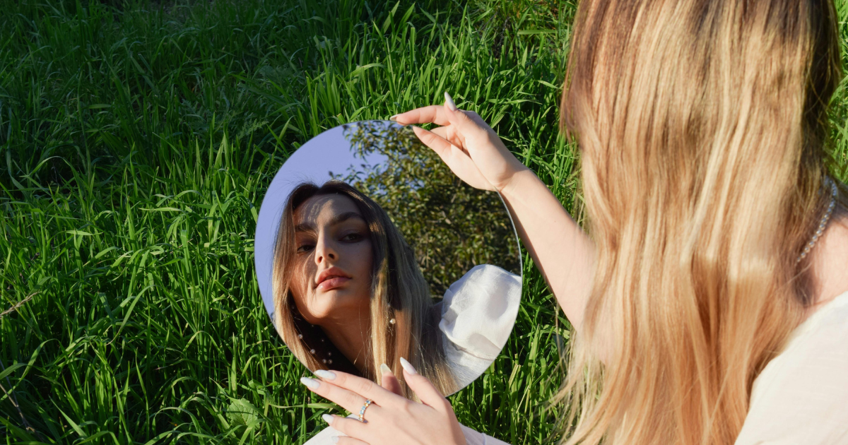 A woman looking at herself in a mirror with self-compassion, emphasizing its importance in letting go of a bitter past.