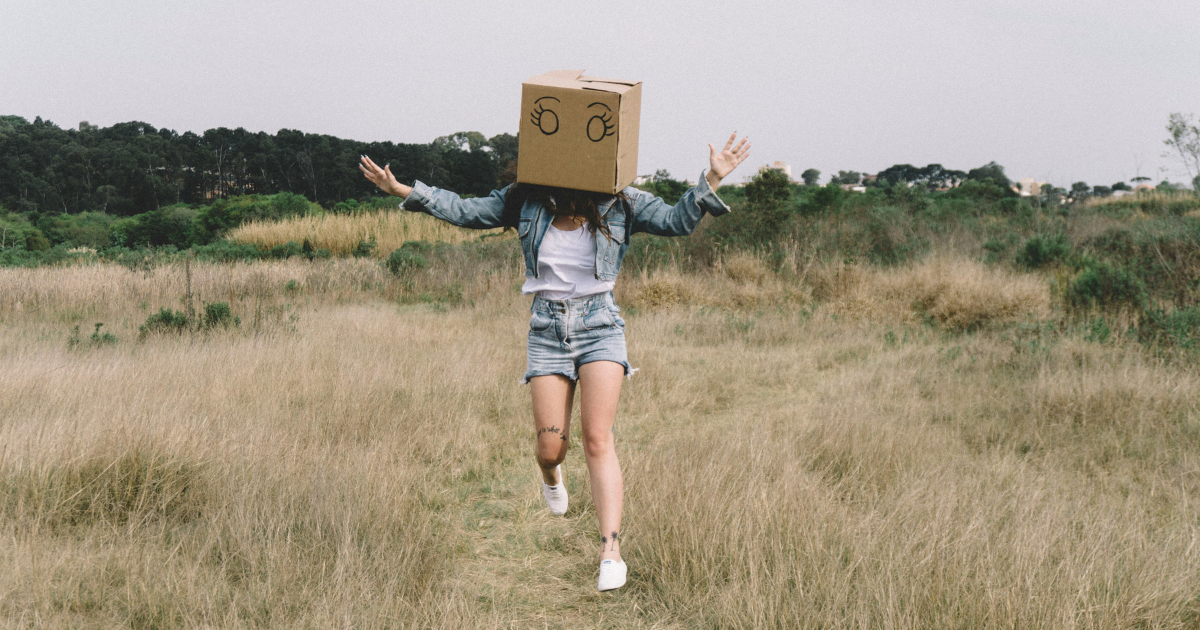 Woman walking with a cardboard box on her head drawn with eyes, adding humor to the concept of letting go.