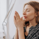 A woman with closed eyes, clasping her hands together in prayer or affirmation, seeking solace and motivation to navigate through the pain of divorce.