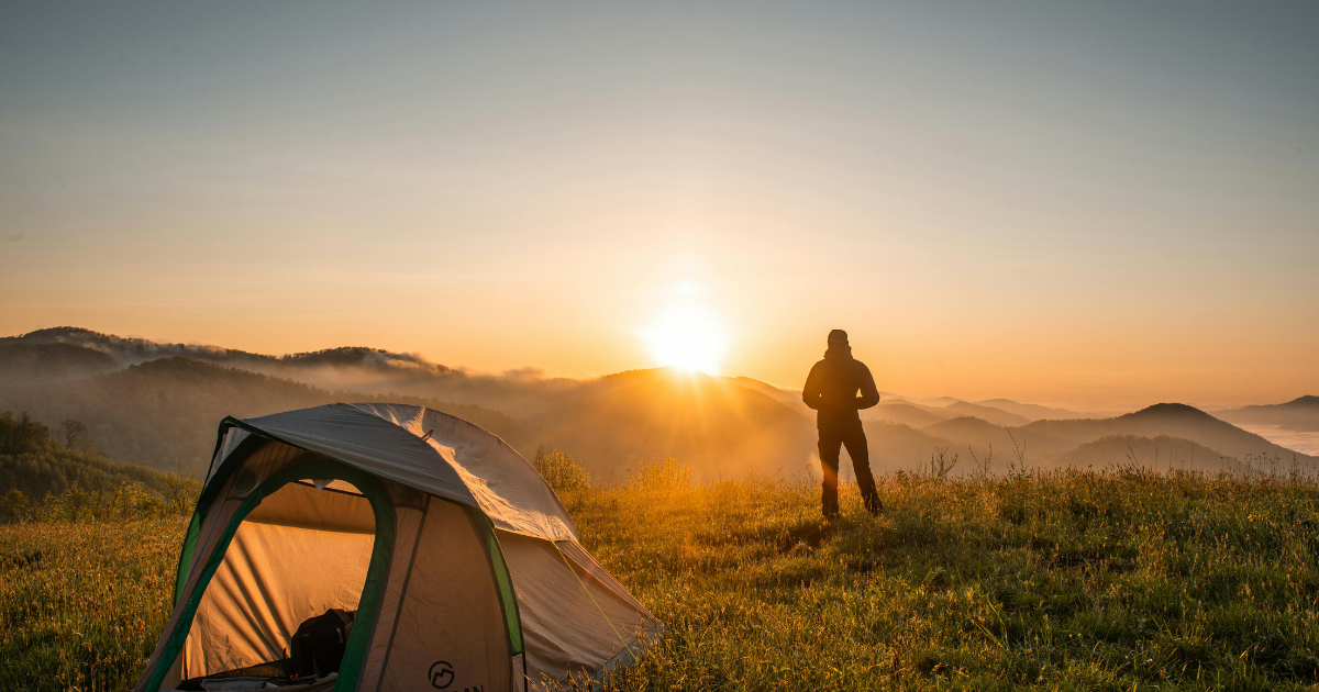 A man standing alone by the side of his tent, contemplating the sunset, symbolizing the choice to explore new experiences rather than resorting to unhealthy coping mechanisms.