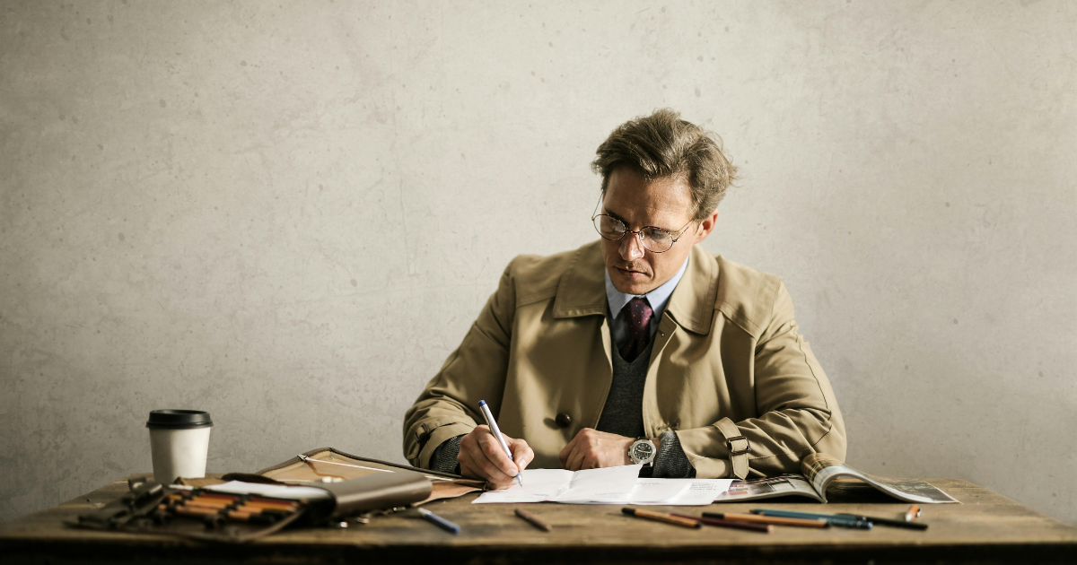 A man seated at a desk, deep in thought, with a pen in hand. He appears to be writing, possibly expressing his feelings or thoughts following a divorce.