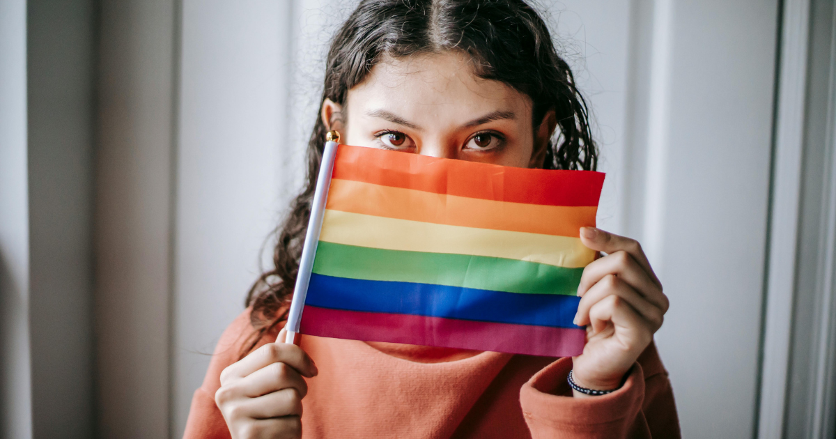 Image: Young girl holding LGBTQ rights flag with intense expression, challenging norms.