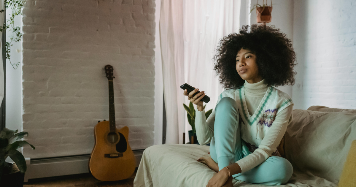 Woman operating TV remote while sitting alone on a bed