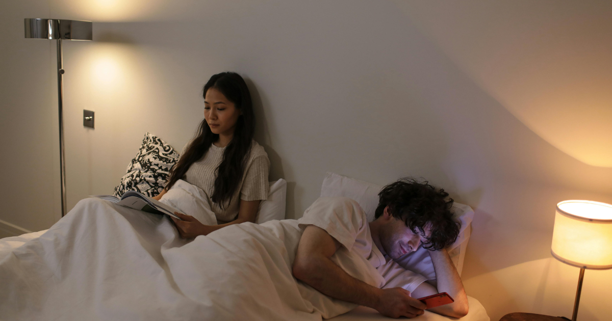 Image of a husband and wife, with the husband engrossed in a screen and the wife absorbed in a book, illustrating the consequences of bed rotting.