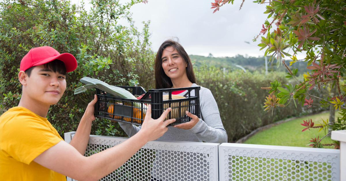 A woman practicing mindful giving, passing a basket of essentials to her young neighbor.