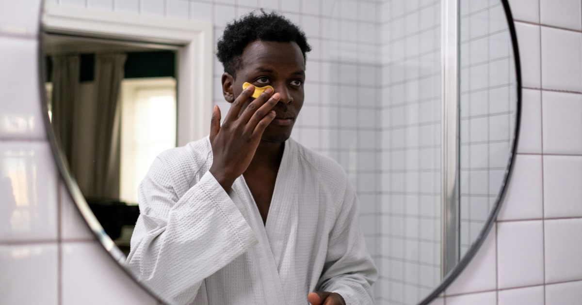 A male model applying under-eye cream as part of his summer skincare routine.