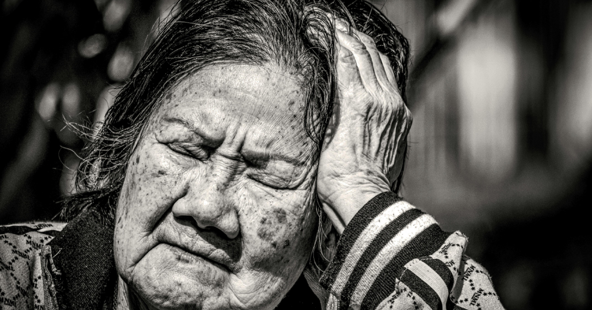 An image of an elderly woman sadly resting her hand on her head, appearing tired due to ageism.