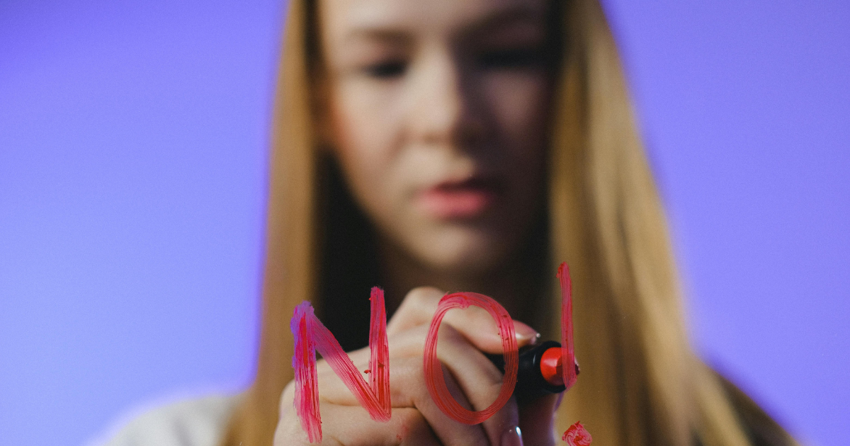 A young man, slightly blurred, writing 'NO' on a glass with lipstick, demonstrating the intensity of expressing refusal.