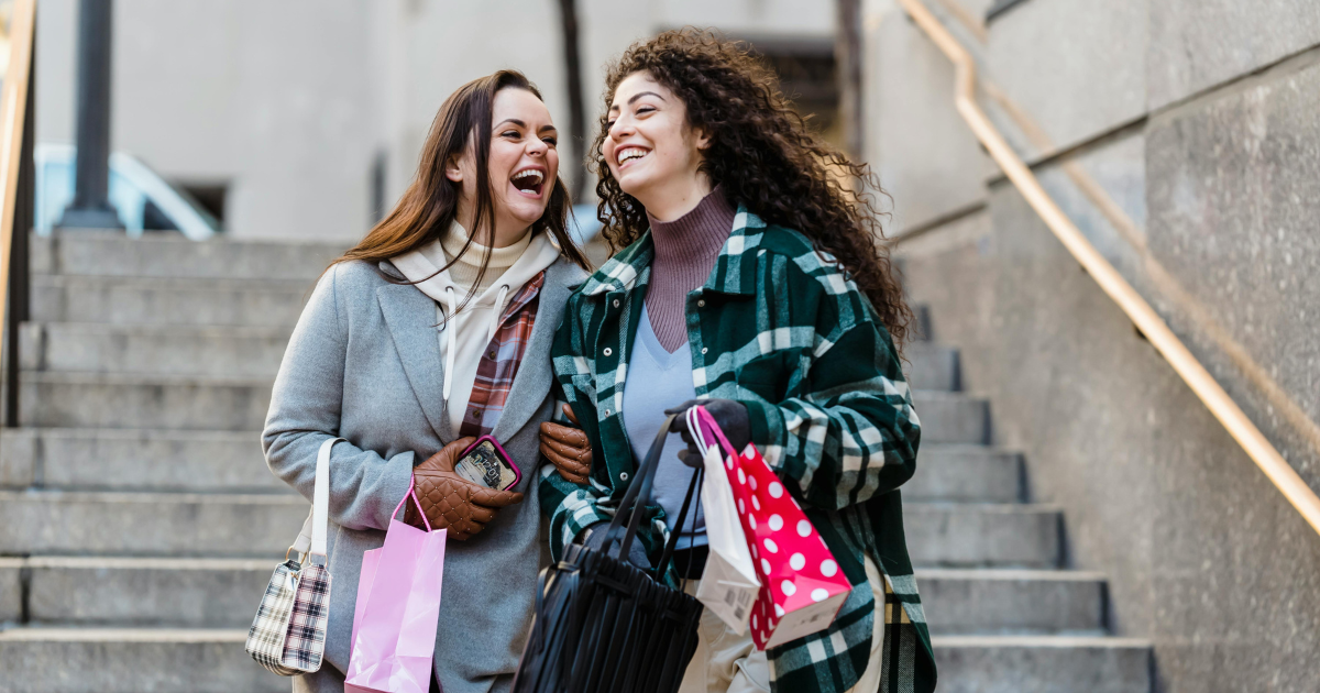 Two young women in a good mood after shopping, smiling and holding shopping bags.