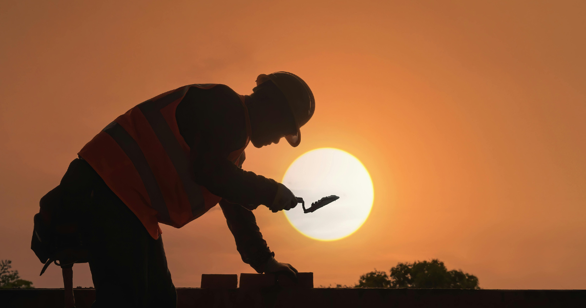 A worker silhouetted against the sun, depicting the hardships of working outdoors during the summer.