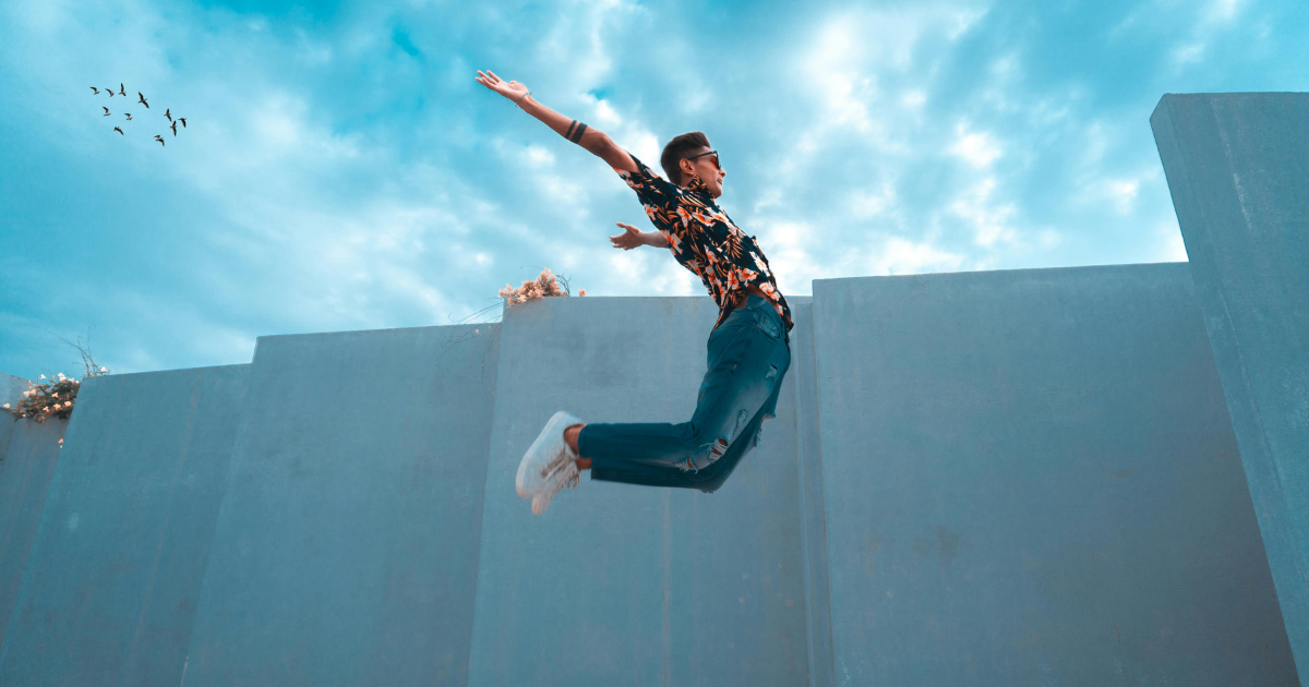 A man jumping high, looking cool in a trendy summer outfit with denim pants, a t-shirt, and white sneakers.