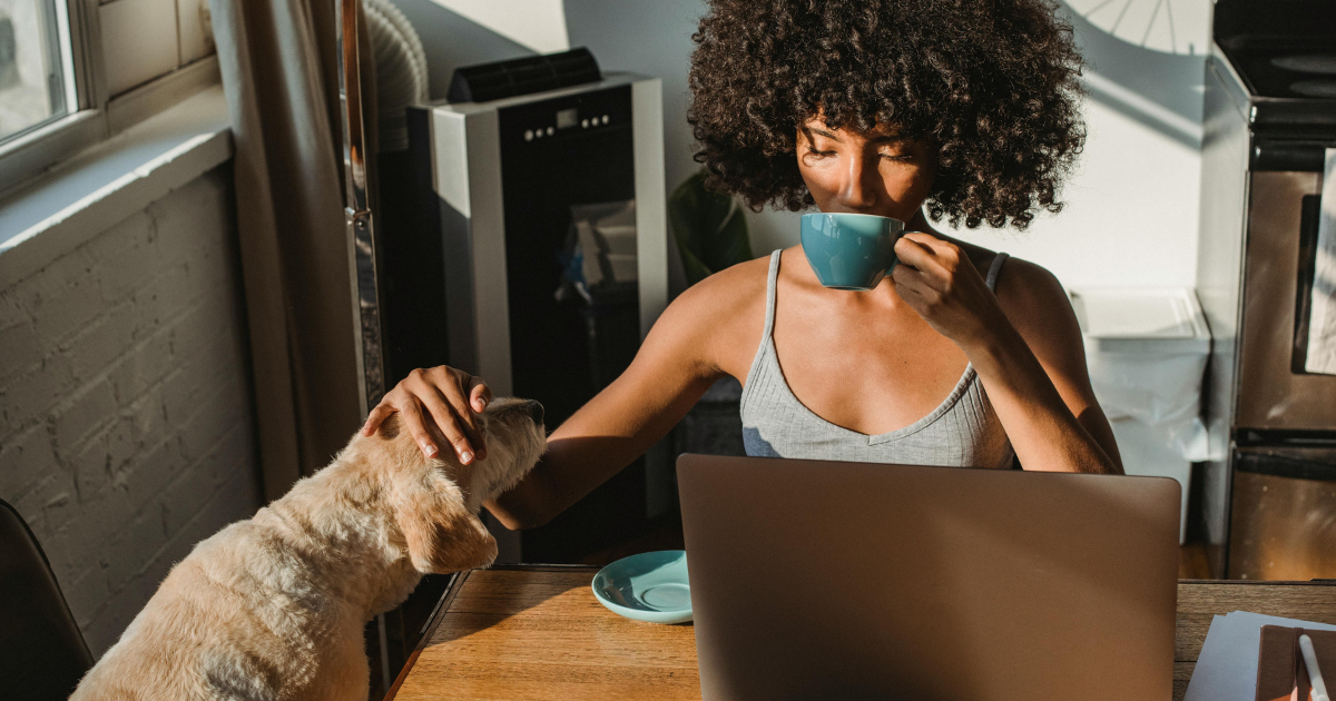 Image of a woman by her laptop, sipping coffee, and patting her pet, illustrating the freedom and independence gained from choosing not to get married.