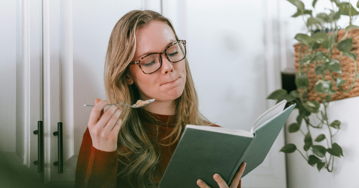 Woman eating and reading alone, capturing the contentment of living alone and the beauty in each moment.