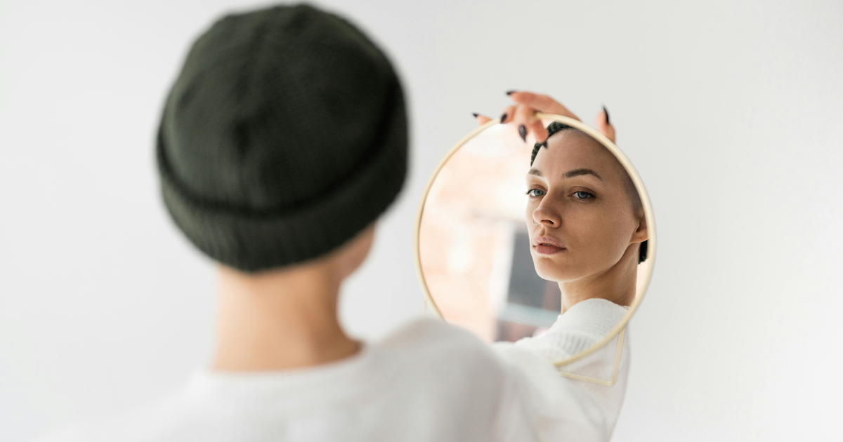 A woman confidently looking at herself in the mirror, embracing her true self and reflecting the essence of being unapologetically you.