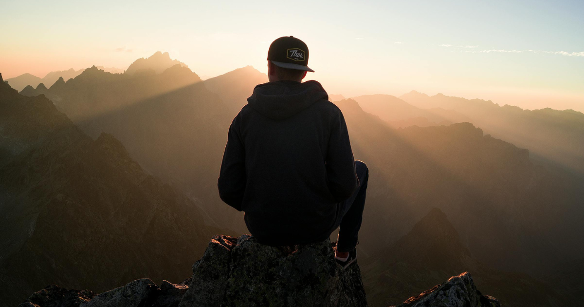 A person sitting on a cliff stone in the evening, introspecting, symbolizes the necessity of self-reflection in finding purpose in life.